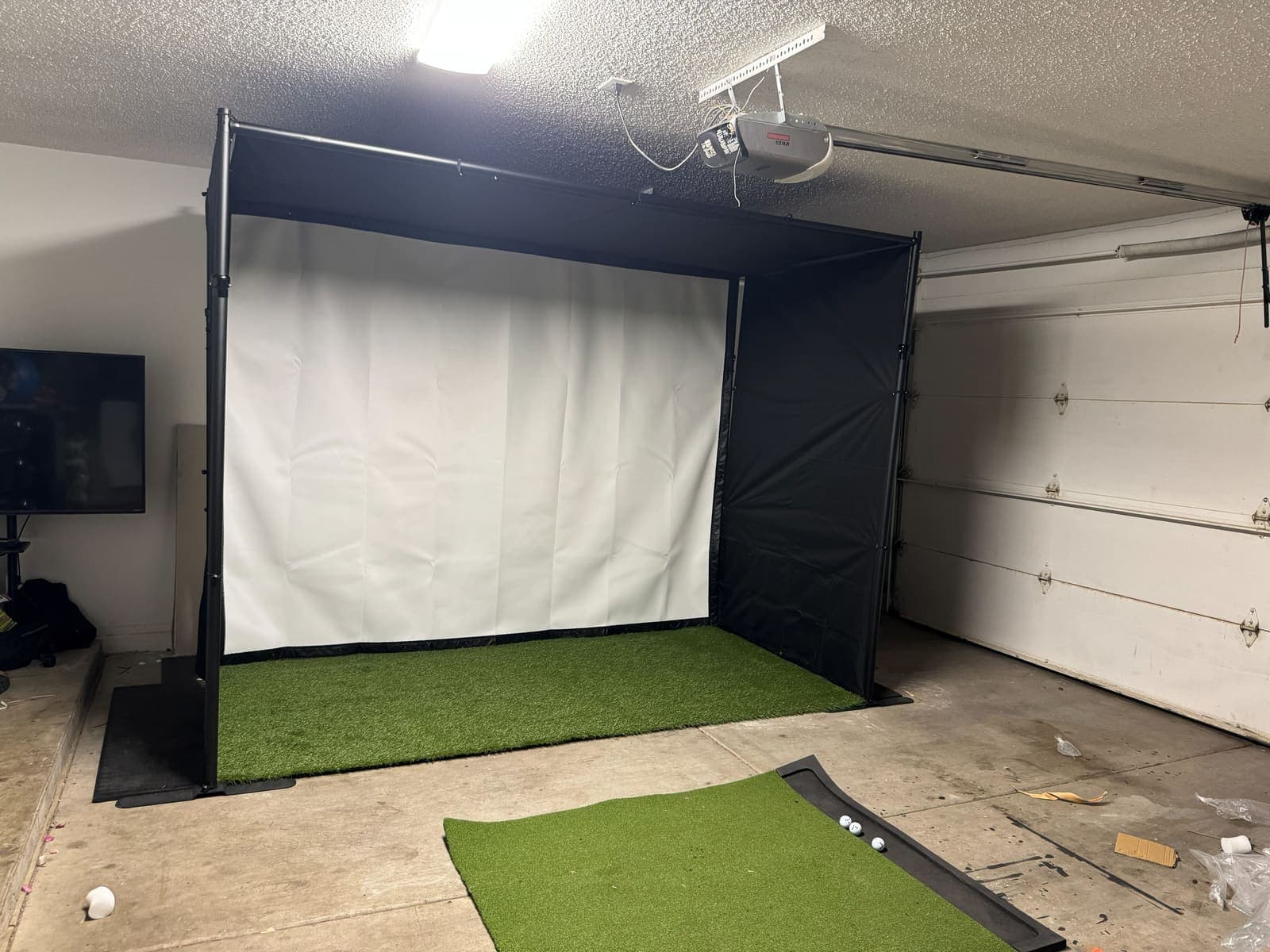 The factory sample deployed in the garage, seen straight on: black shell panels, white impact screen, the full ten foot bay. Phone photo, October 10, 2026.