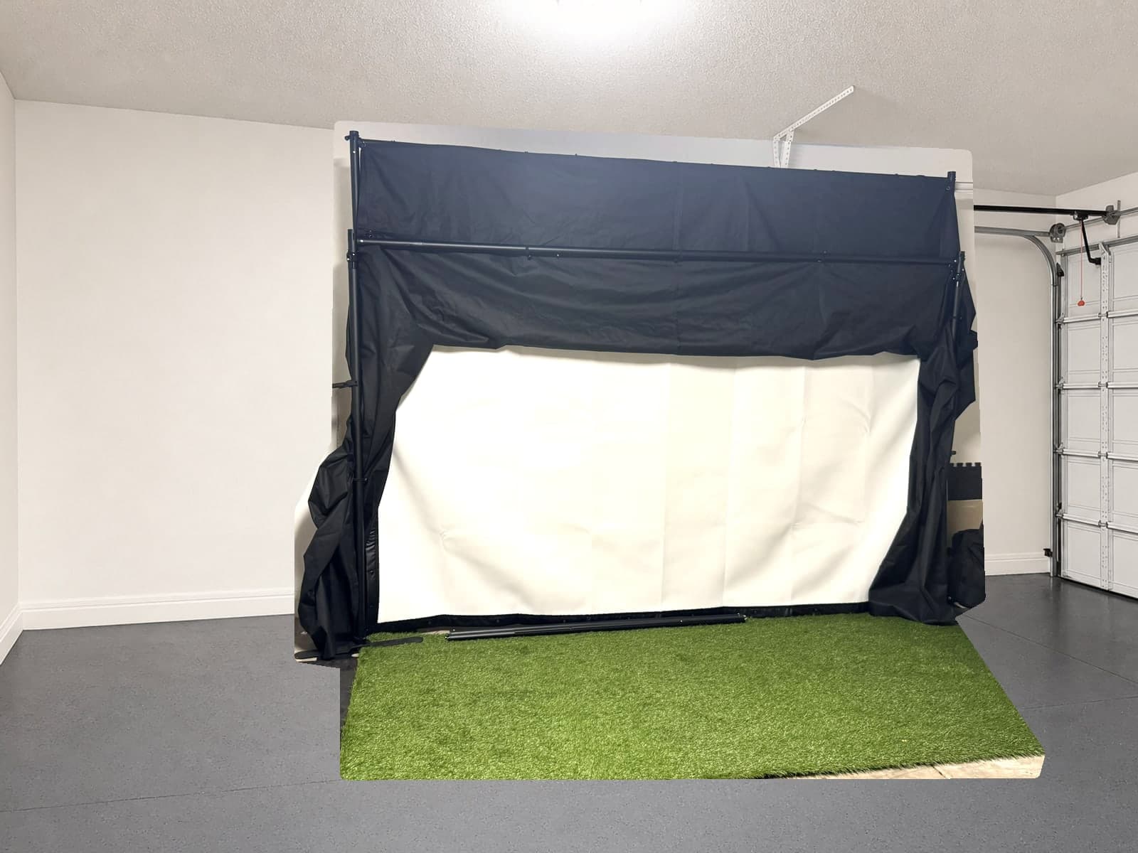 The factory sample folded flat against the garage wall with the impact screen still standing and the floor in front of it empty. Photo, Oct 10, 2026, background cleaned