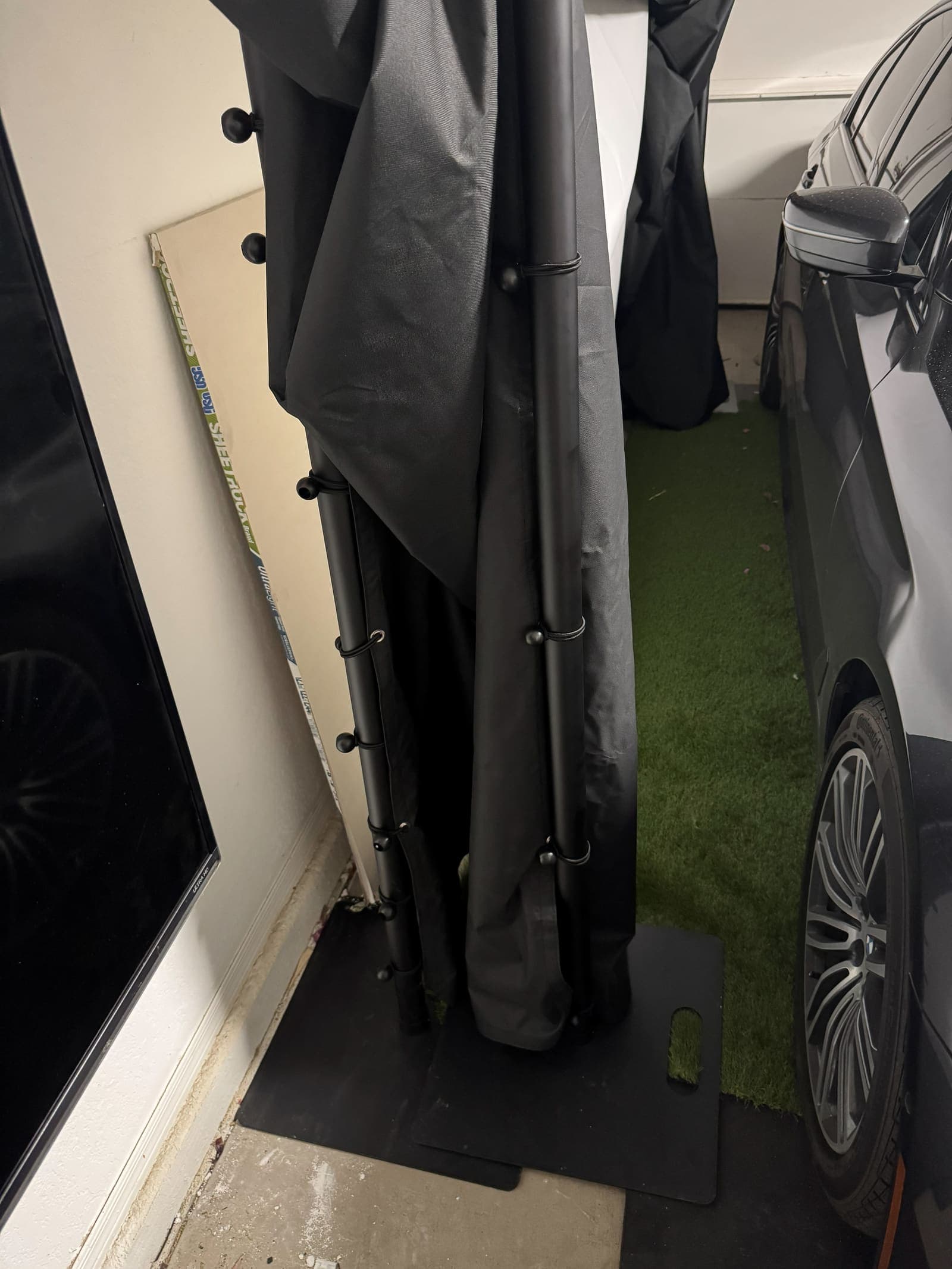 The factory sample folded against the garage wall with the car parked beside it. Phone photo, October 11, 2026.