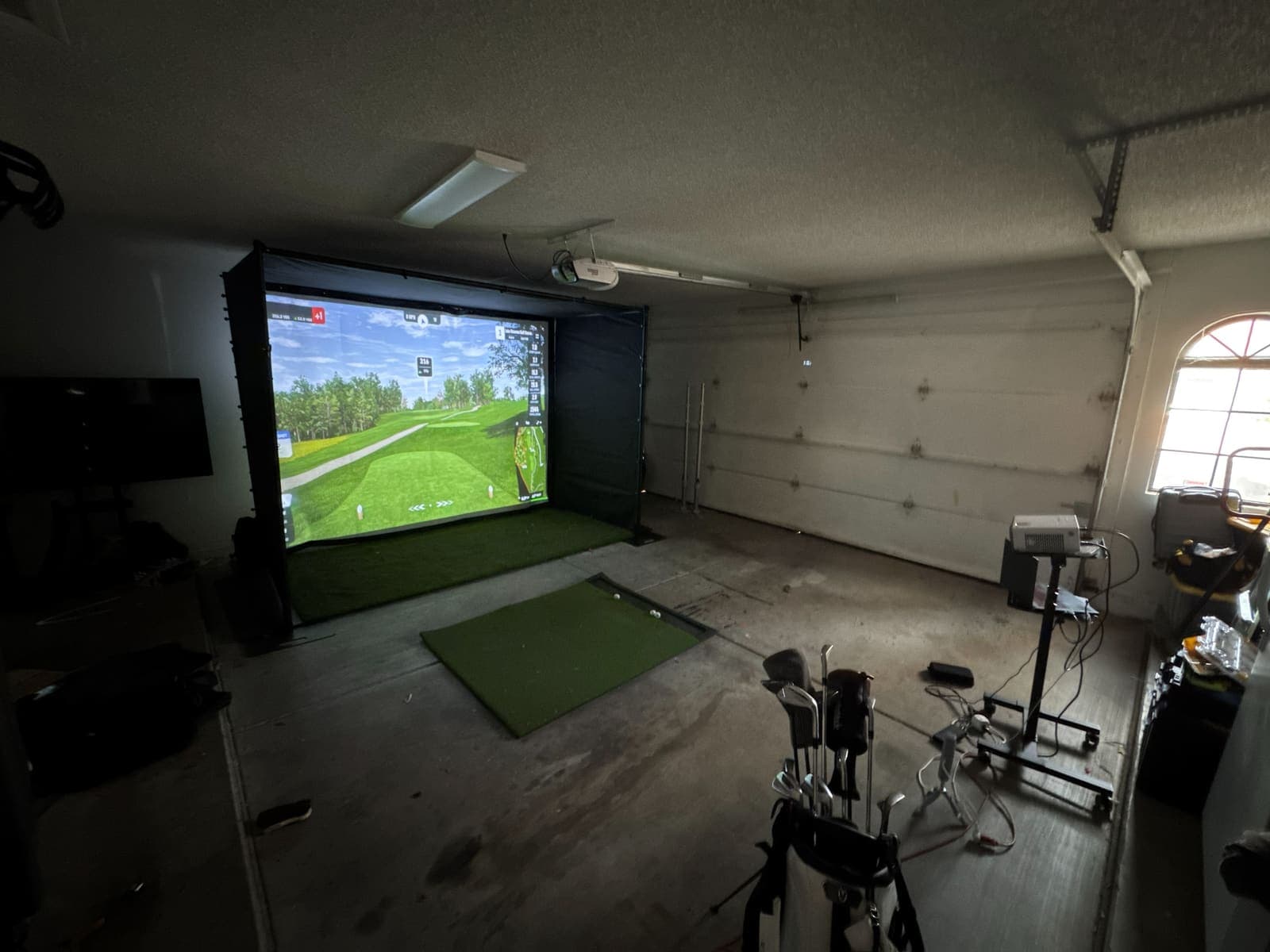 The two-car garage with the factory sample deployed and a GSPro course on the screen. Phone photo, October 11, 2026.